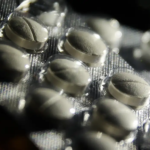 Imagem em close de uma cartela de pílulas de remédios brancos.