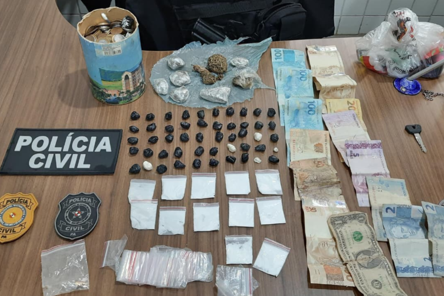 Na imagem aparece uma mesa onde estão todas as apreensões realizadas, com papelotes de substância análoga ao crack, nove papelotes maiores de substância semelhante à maconha e outros 12 papelotes de material análogo à cocaína. Além disso, tem dinheiro em espécie, uma lata cheia de moedas e os selos da Polícia Civil.