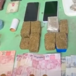 Na imagem estão as apreensões sobre uma mesa de plástico verde, com celulares, dinheiro em espécie, balança de precisão e drogas.