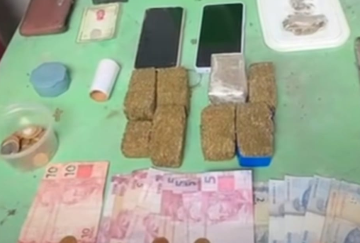 Na imagem estão as apreensões sobre uma mesa de plástico verde, com celulares, dinheiro em espécie, balança de precisão e drogas.