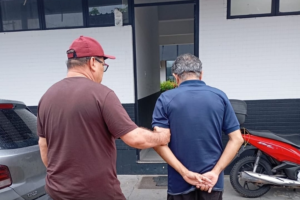 Imagem de um agente da Polícia Civil sem farda conduzindo o suspeito até a delegacia.