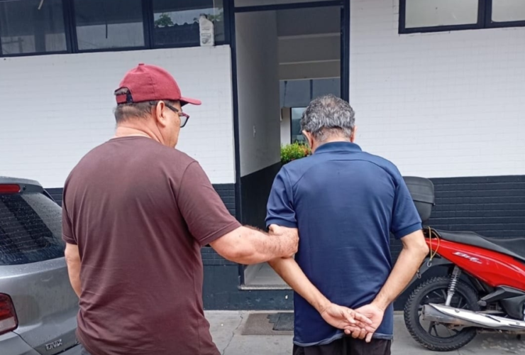 Imagem de um agente da Polícia Civil sem farda conduzindo o suspeito até a delegacia.