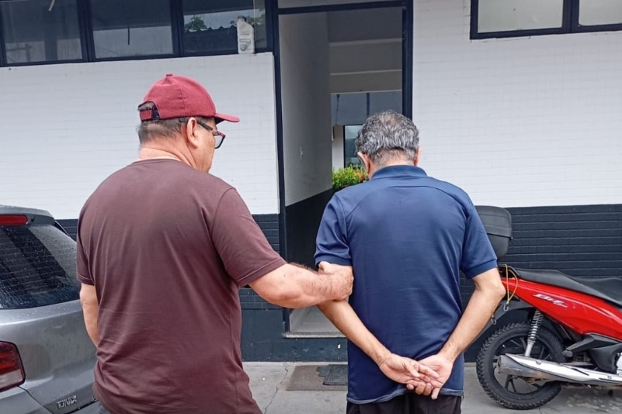 Imagem de um agente da Polícia Civil sem farda conduzindo o suspeito até a delegacia.