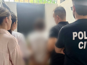 Na imagem aparece agentes da polícia civil deslocando o suspeito, sendo duas agentes mulheres e dois homens fardados. A imagem do suspeito aparece borrada.