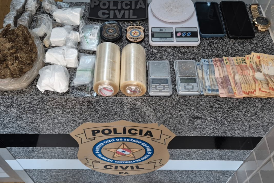 Na imagem aparece as apreensões sobre uma mesa de mármore, nela estão balaças de precisão, quantia em dinheiro, 2 rolos de plástico filme, drogas, além do selo da polícia civil.