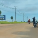 A imagem é um recorte do vídeo onde um homem aparece se deslocando com uma criança em uma motocicleta em uma estrada.