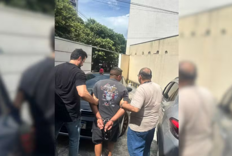 Na imagem o suspeito aparece de costas algemado, enquanto dois agentes da Polícia Civil sem farda o conduzem em meio a um estacionamento com veículos.