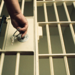 Imagem ilustrativa de uma sela de polícia com uma mão fechando com as chaves a grade.