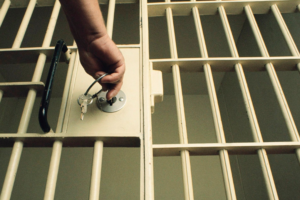 Imagem ilustrativa de uma sela de polícia com uma mão fechando com as chaves a grade.