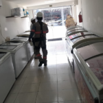 Imagem da operação no interior do estabelecimento com dois agentes fiscalizando em um corredor repleto de refrigeradores.