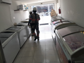 Imagem da operação no interior do estabelecimento com dois agentes fiscalizando em um corredor repleto de refrigeradores.