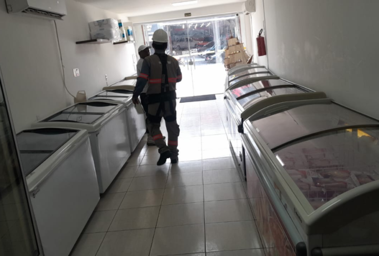 Imagem da operação no interior do estabelecimento com dois agentes fiscalizando em um corredor repleto de refrigeradores.
