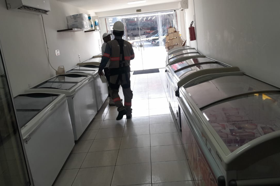 Imagem da operação no interior do estabelecimento com dois agentes fiscalizando em um corredor repleto de refrigeradores.