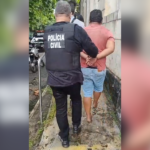 Na imagem, um agente da Polícia Civil conduzindo o suspeito algemado até uma unidade policial.