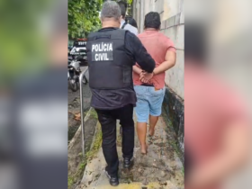 Na imagem, um agente da Polícia Civil conduzindo o suspeito algemado até uma unidade policial.