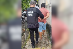 Na imagem, um agente da Polícia Civil conduzindo o suspeito algemado até uma unidade policial.