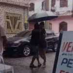 Casal dançando na chuva enquanto segura uma sombrinha