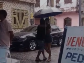 Casal dançando na chuva enquanto segura uma sombrinha