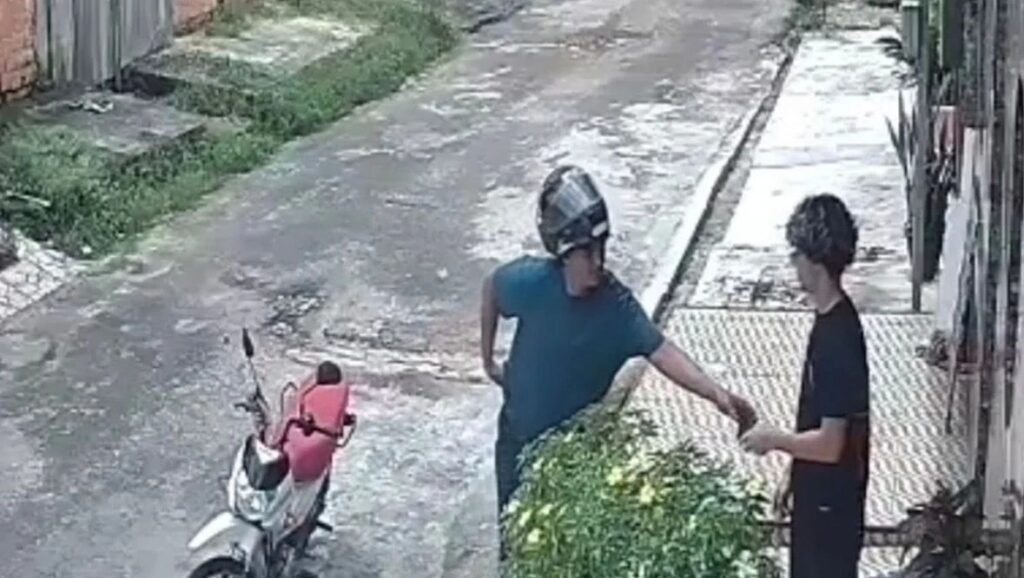 Assaltante aborda o jovem na calçada durante o assalto.