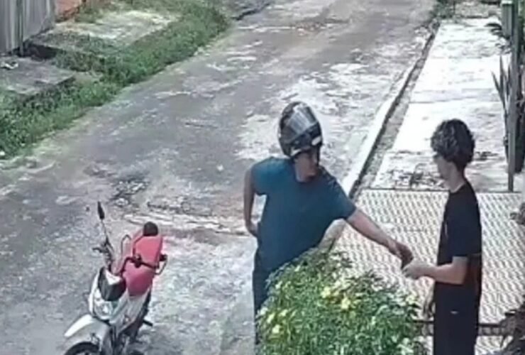 Assaltante aborda o jovem na calçada durante o assalto.