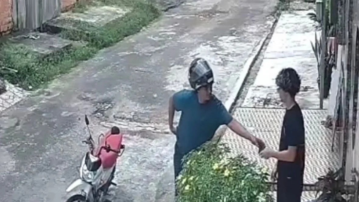 Assaltante aborda o jovem na calçada durante o assalto.