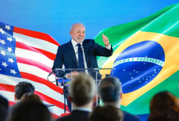Presidente lula em pé com a bandeira do brasil e do EUA atras