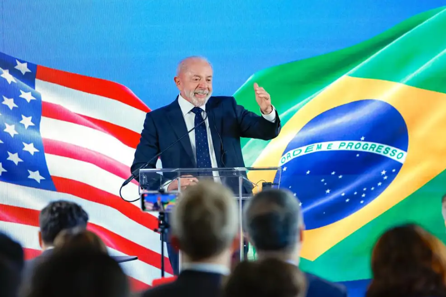 Presidente lula em pé com a bandeira do brasil e do EUA atras