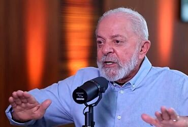 Lula em foto de destaque com os braços abertos e um microfone de podcast