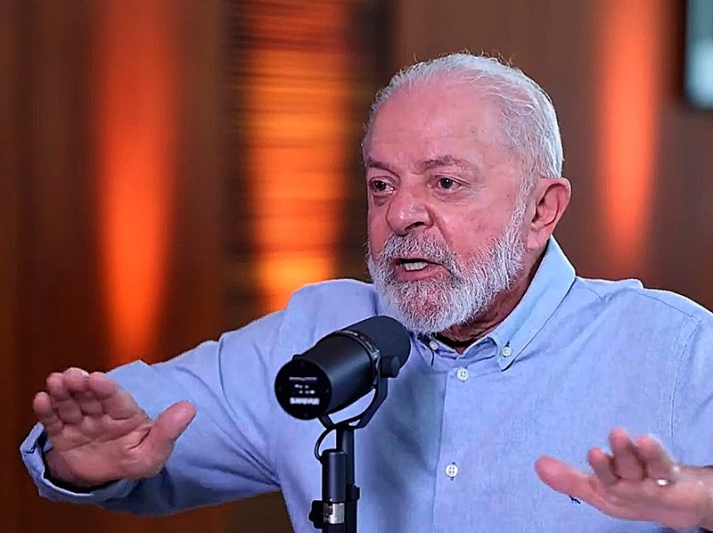 Lula em foto de destaque com os braços abertos e um microfone de podcast